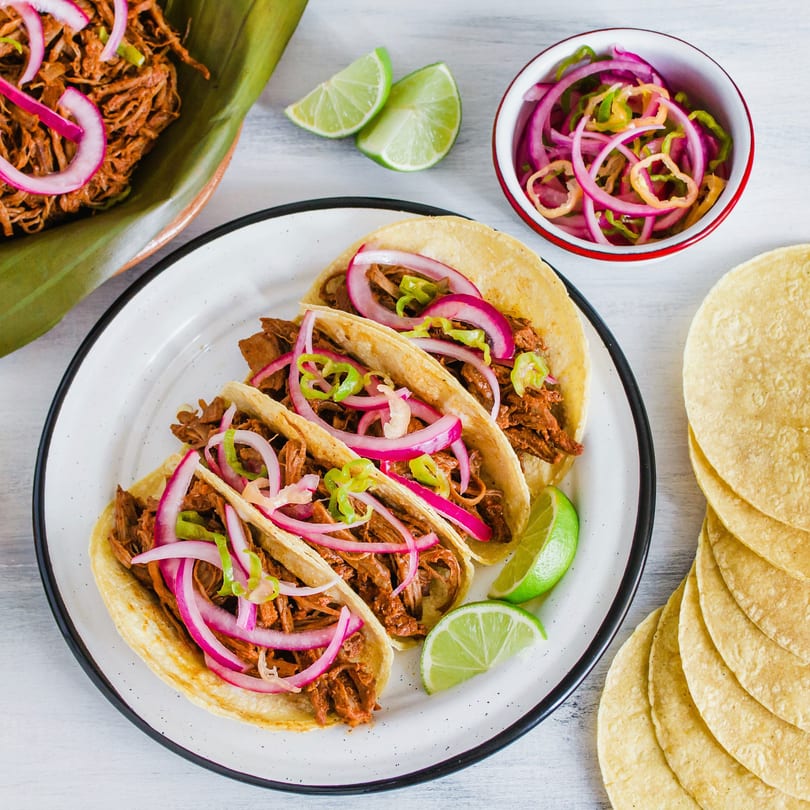 Maestros’s Mexican grill tacos with shredded meat, red onions, green peppers, and lime wedges.