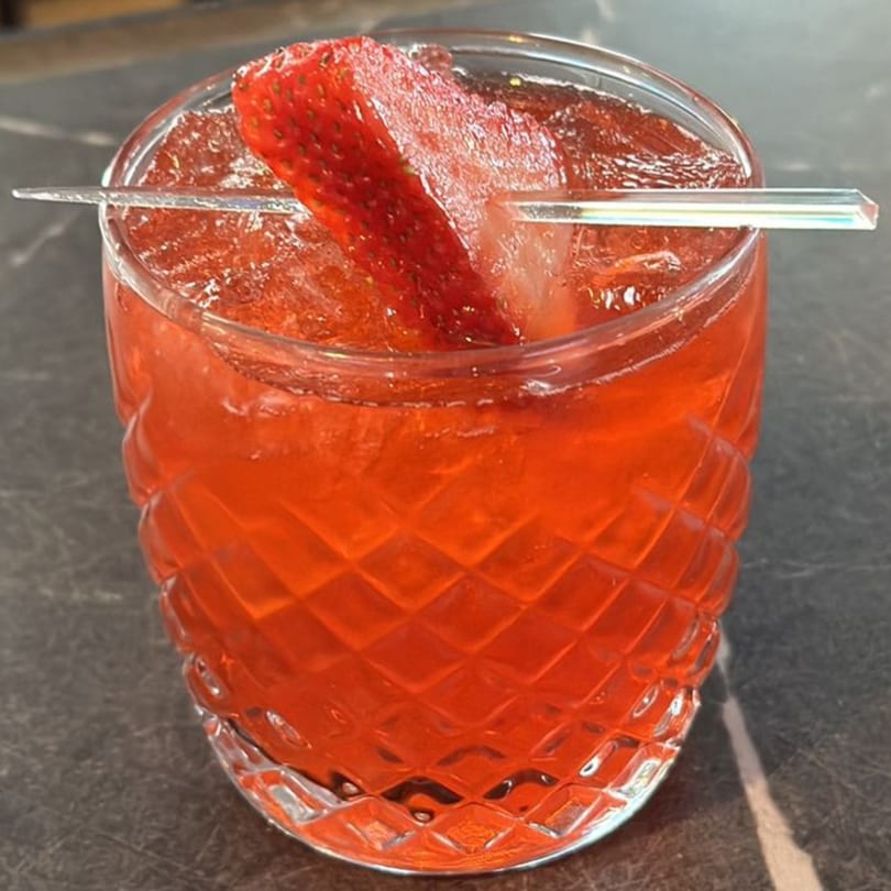 A vibrant red strawberry margarita in a textured glass, garnished with a fresh strawberry slice.